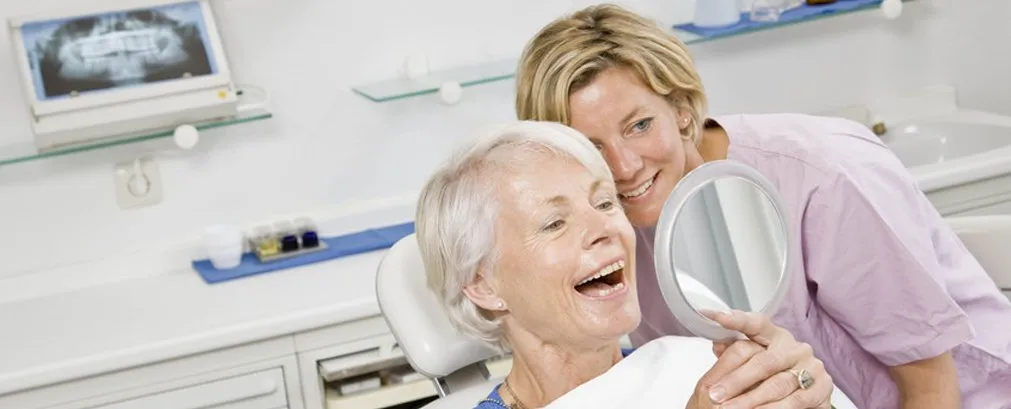 Lady smiling, holding mirror, with technician